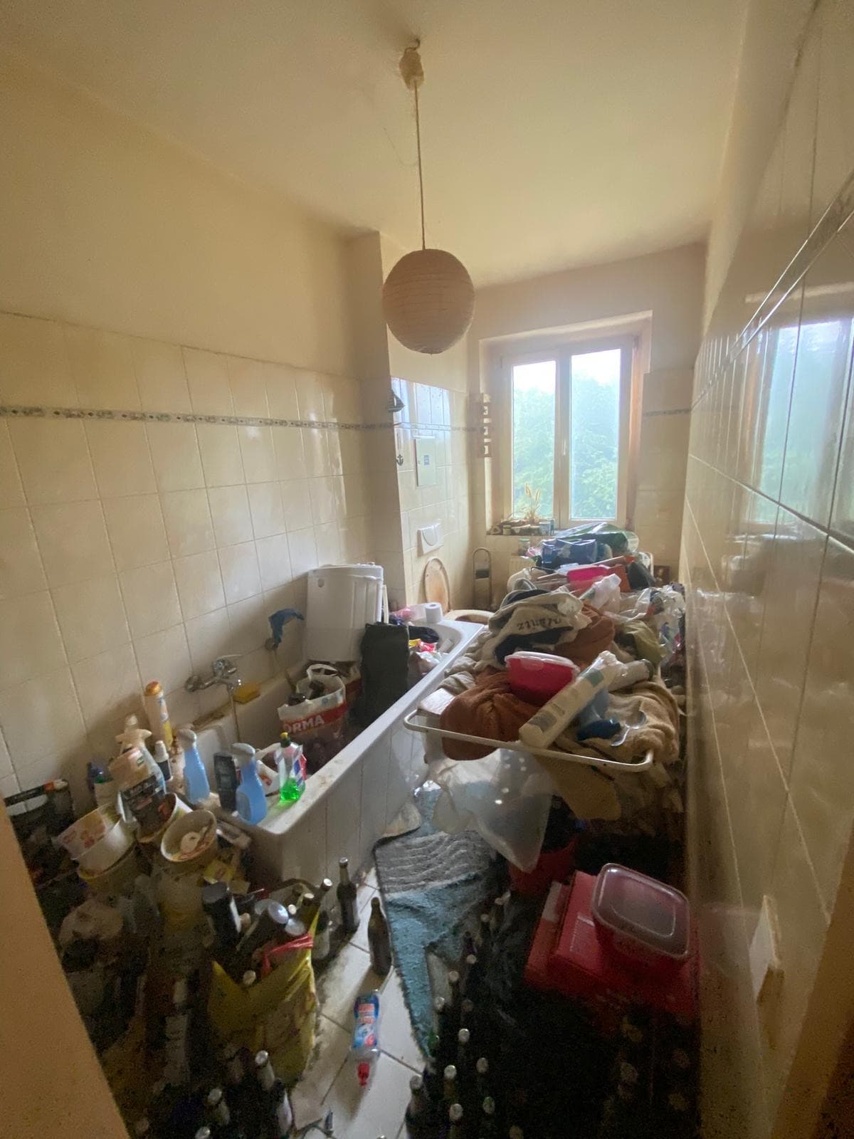 Vollständig zugestelltes Badezimmer vor der Haushaltsauflösung, Wanne und Boden voller Flaschen und Hausrat