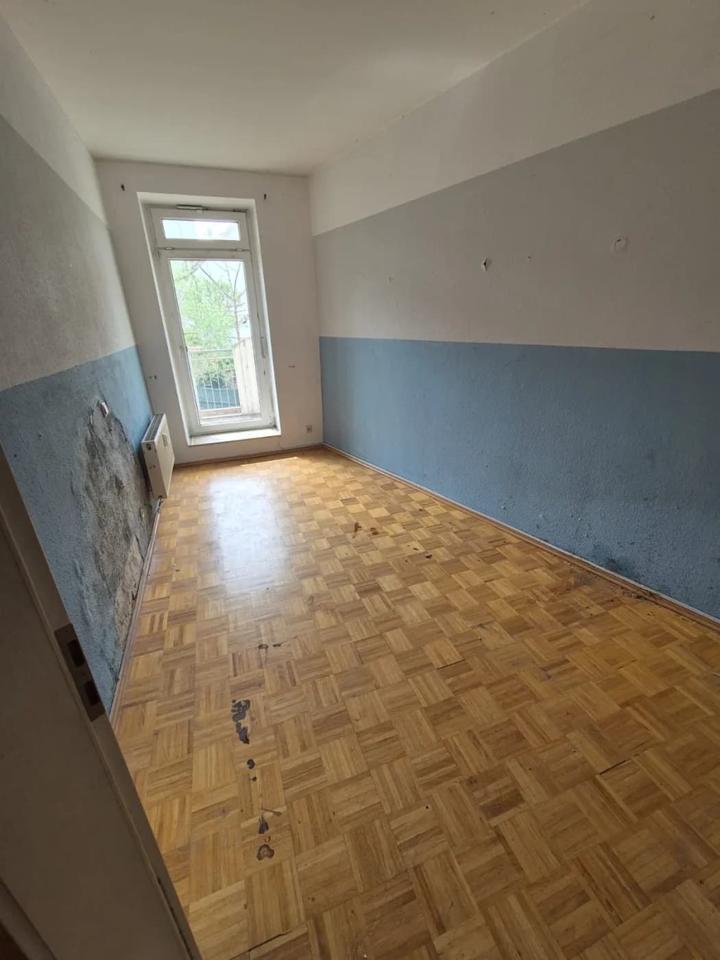 Dasselbe Zimmer geräumt und übergabefertig, blau-weisse Wand, freies Parkett